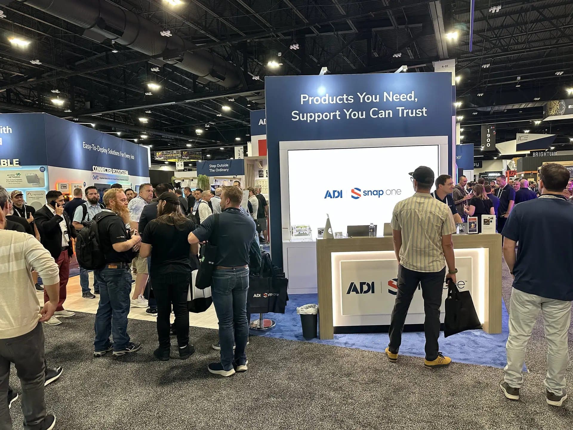 A crowd at the ADI Global trade show booth, in front of its video wall and demo counter