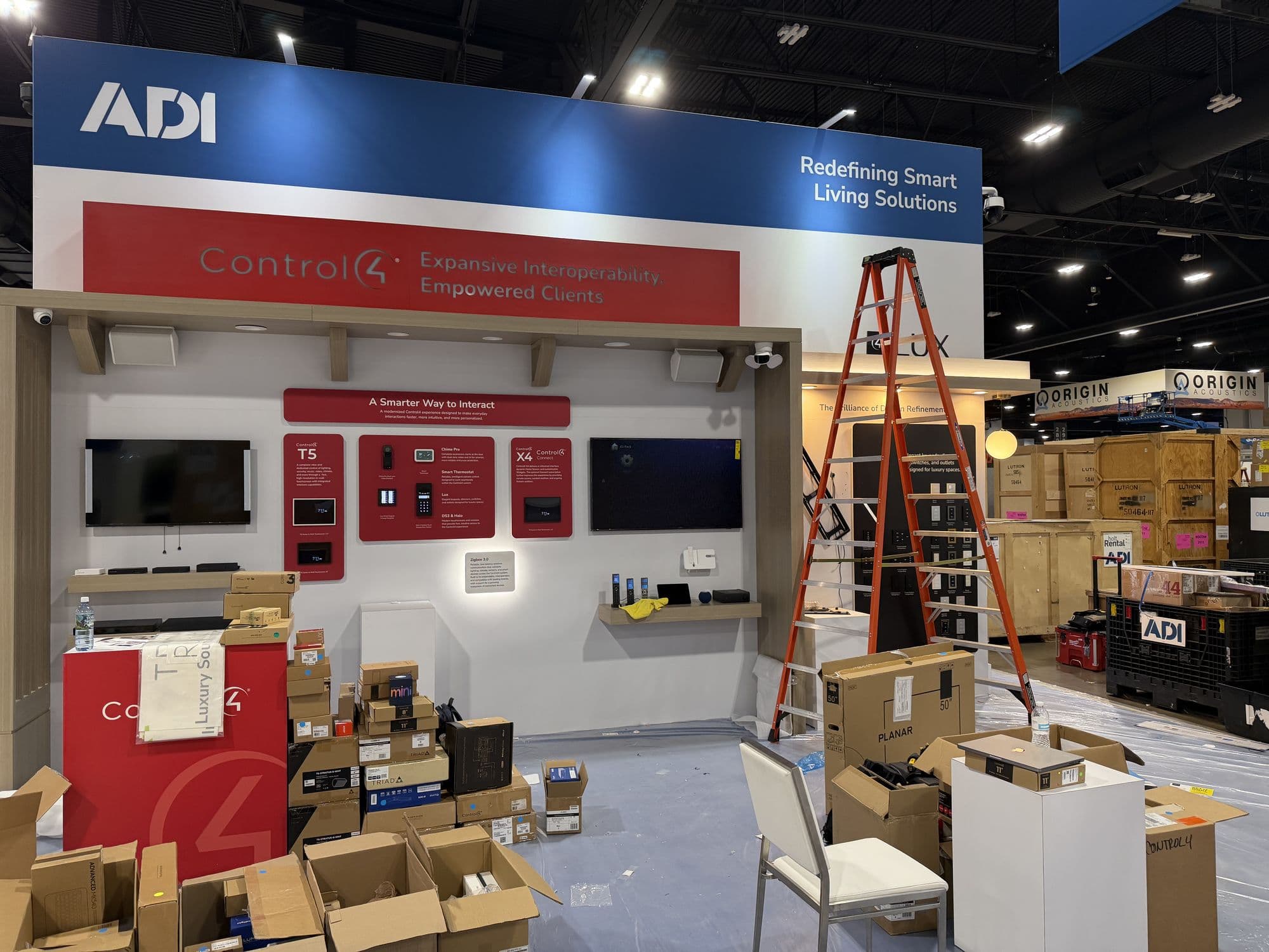 A trade show booth being built: displays on the wall, ladders, cases and boxes on the floor