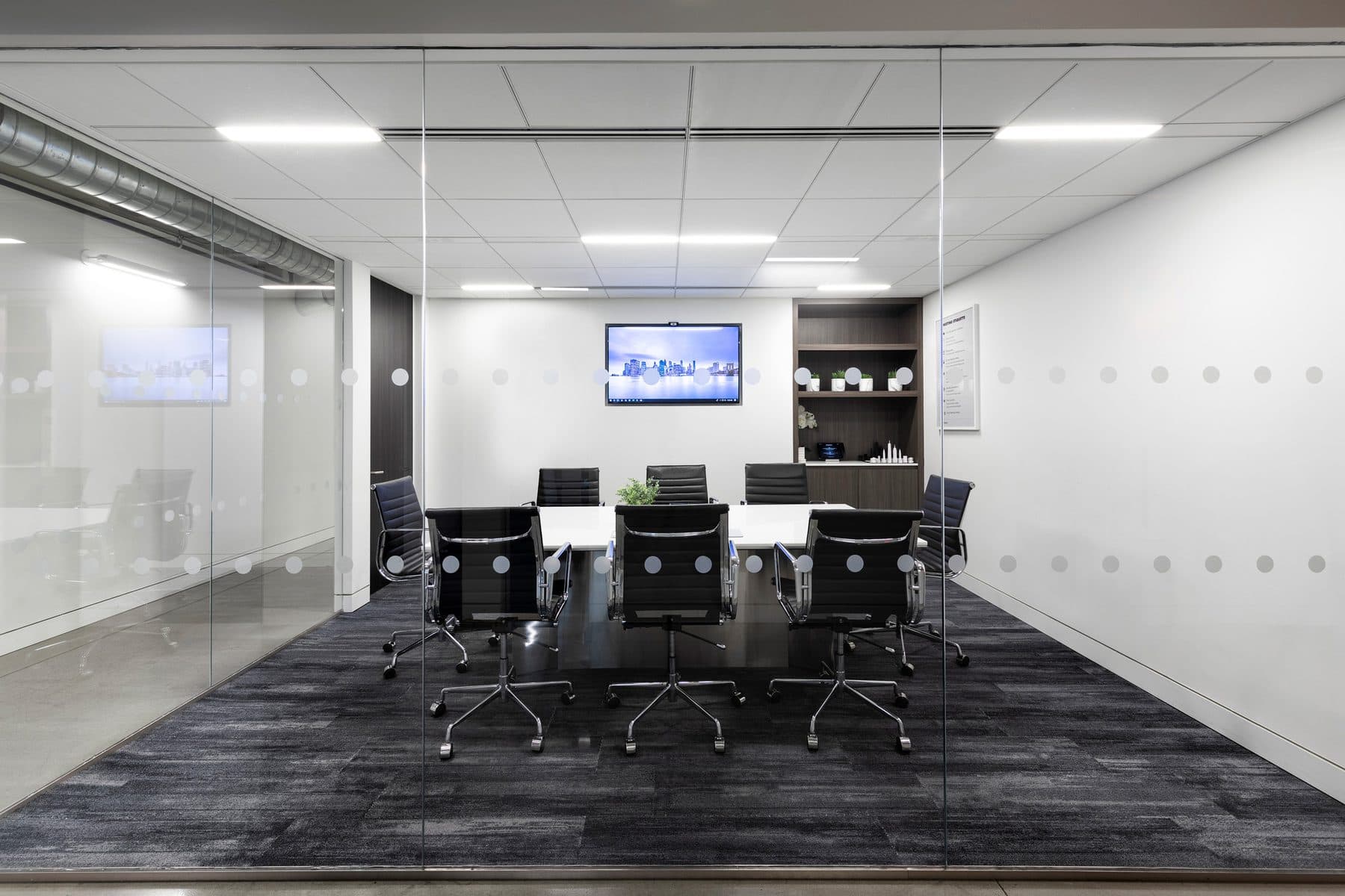 A glass-walled conference room with a display on the end wall