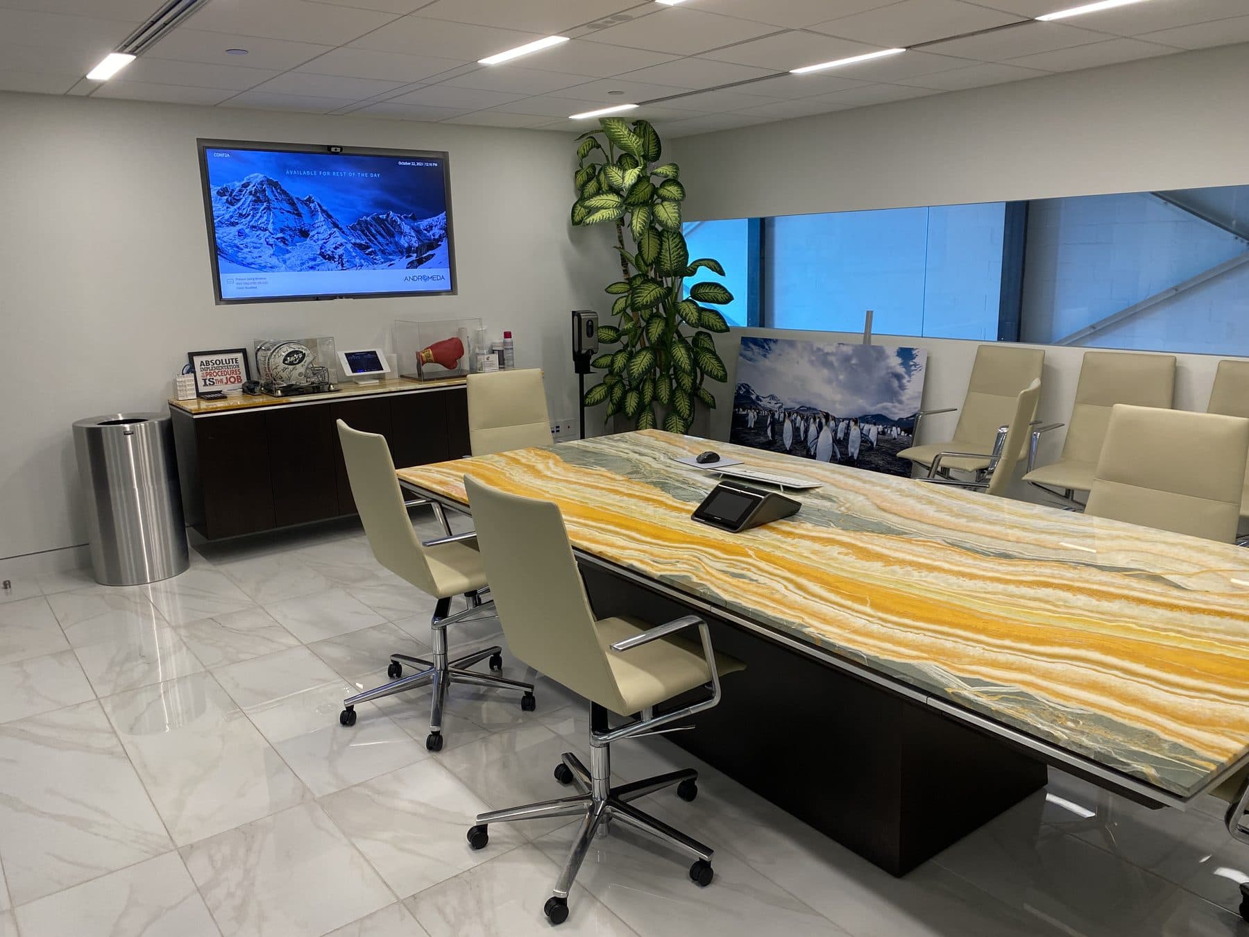 A conference room with a marble table, a display on the wall and a touch panel on the table